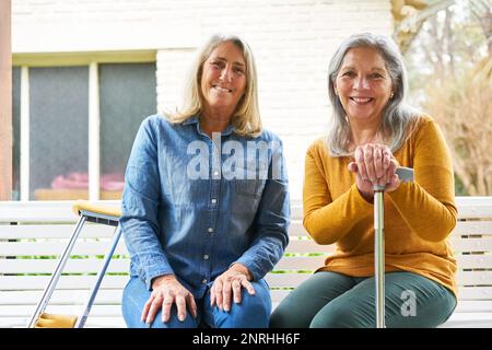 Porträt einer glücklichen älteren Frau, die mit einer Freundin auf einer Bank im Garten sitzt Stockfoto