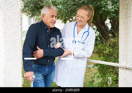 Lächelnde junge Pflegekraft, die behinderten älteren Mann beim Gehen im Garten unterstützt Stockfoto