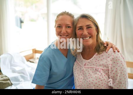 Portrait einer lächelnden Pflegekraft, die eine bettsitzende ältere Frau im Rehabilitationszentrum umarmt Stockfoto