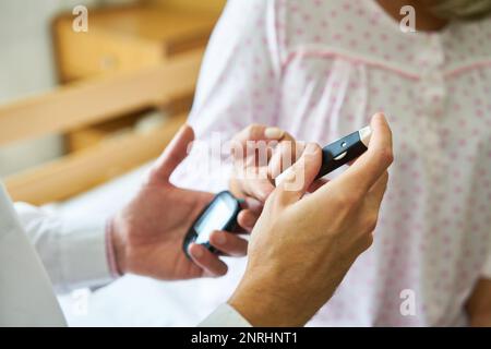 Nahaufnahme einer Krankenschwester zur Blutzuckerkontrolle am Finger eines Diabetikers im Seniorenheim Stockfoto