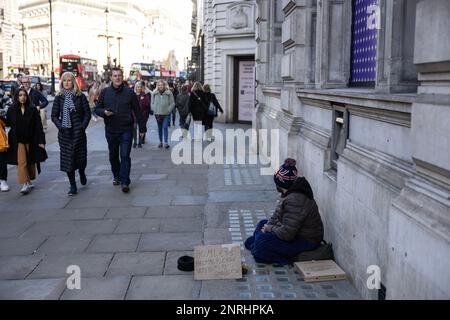 Ein Obdachloser sitzt auf dem Bürgersteig mit einem Schild, auf dem er um Hilfe mit Essen oder Geld bittet, Piccadilly, London, England, Großbritannien Stockfoto