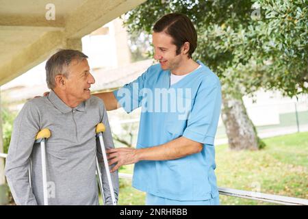 Lächelnde Krankenschwester, die ältere Menschen mit Behinderung beim Gehen im Garten unterstützt Stockfoto