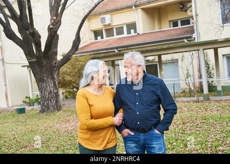 Glückliches Seniorenpaar, das im Herbst Hand in Hand im Garten des Pflegeheims steht Stockfoto