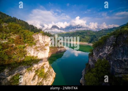 Blick von einer Brücke in der Nähe des Castel Cagno auf den See Lago di Santa Giustina, Gipfel der Maddalene Bergkette in der Ferne. Stockfoto