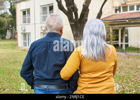Rückansicht eines älteren Paares, das Hand in Hand im Garten des Pflegeheims steht Stockfoto