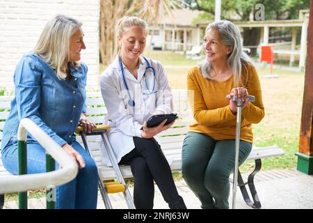 Lächelnde Krankenschwester erklärt ältere Frauen über Tablet-PC im Garten eines Pflegeheims Stockfoto