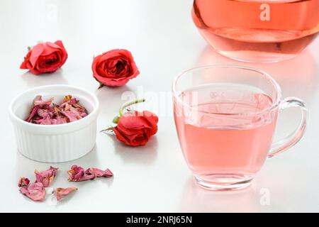 Rose Tea in einem Glasbecher mit getrockneten Rosen im Hintergrund Stockfoto