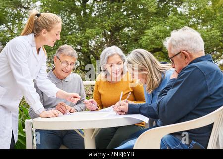 Gruppe glücklicher Seniorenfreunde löst Kreuzworträtsel und Labyrinth im Pflegegarten home0 Stockfoto