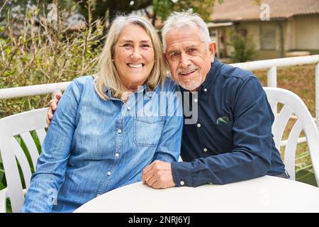 Porträt eines fröhlichen Seniorenmannes und einer Frau, die im Garten des Pflegeheims am Tisch sitzt Stockfoto