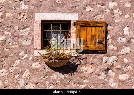 Kleines Fenster in der Steinmauer eines traditionellen Bauernhauses in einem kleinen Dorf mit Bars, Fensterläden und einem Terrakotta-Blumentopf. Stockfoto