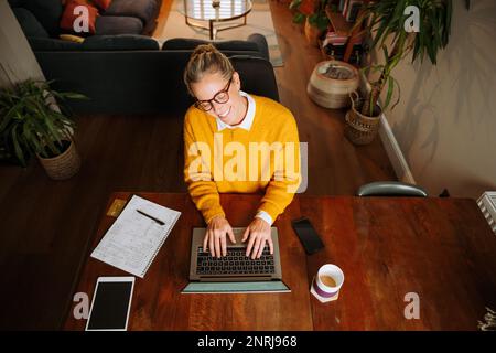 Eine weiße Frau, die von zu Hause aus arbeitet und auf einem Laptop tippt Stockfoto