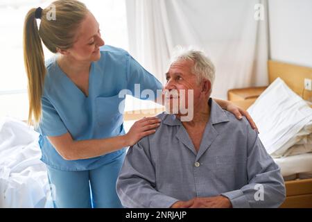 Lächelnde Krankenschwester umarmt Senioren, die im Rollstuhl im Reha-Zentrum sitzen Stockfoto