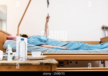 Homecare verstellbares elektrisches Krankenhausbett mit Kranker Haltegriff und Tisch mit Medizin im Vordergrund zu Hause Stockfoto