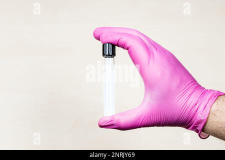 Handschuhe halten geschlossenes Reagenzglas mit weißer, durchsichtiger Flüssigkeit über dem beleuchteten Schreibtisch mit Kopierraum Stockfoto