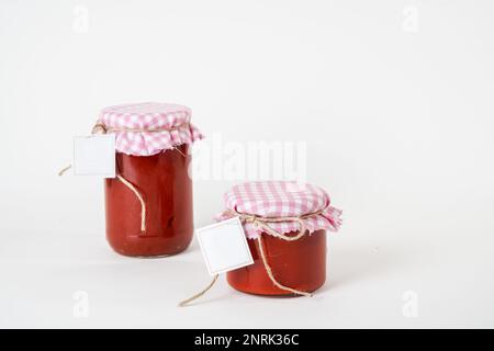 Zwei Dosen mit hausgemachter Tomatenpaste und leeren Etiketten, isoliert auf weißem Hintergrund Stockfoto