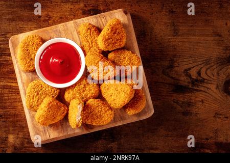 Chicken Nuggets mit Ketchup auf dunklem Holzhintergrund, von oben mit Kopierbereich aufgenommen. Eine knusprige Vorspeise in einem Restaurant, Fingerfood Stockfoto