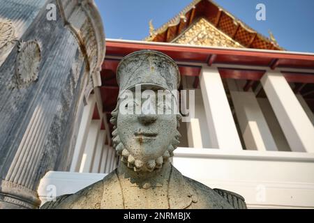 Eine mehr als lebensgroße Steinstatue eines bärtigen europäischen Soldaten des 19. Jahrhunderts, der Wat Suthat (Tempel) in Bangkok, Thailand, bewacht Stockfoto
