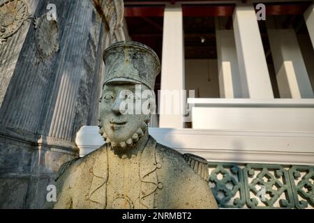 Eine mehr als lebensgroße Steinstatue eines bärtigen europäischen Soldaten des 19. Jahrhunderts, der Wat Suthat (Tempel) in Bangkok, Thailand, bewacht Stockfoto