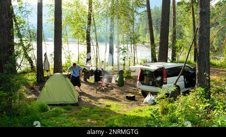 Ein Mann läuft zwischen einem Auto und einem Touristenzelt auf einem Parkplatz im Wald im Altai-Gebirge in der Nähe des Flusses. Stockfoto