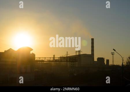 Fabrikgebäude und Rohre eines kohlebefeuerten Wärmekraftwerks am Stadtrand bei Sonnenuntergang in Russland. Stockfoto