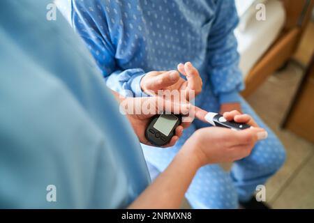 Nahaufnahme einer Krankenschwester zur Blutzuckerkontrolle am Finger eines Diabetikers im Pflegeheim Stockfoto