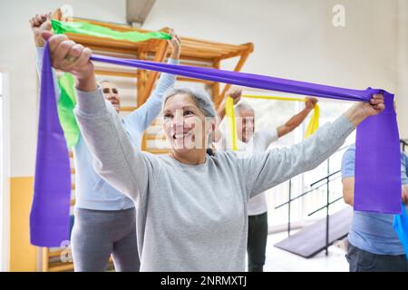 Lächelnde Seniorin und Männer beim Training mit Stretch-Bändern im Rehabilitationszentrum Stockfoto