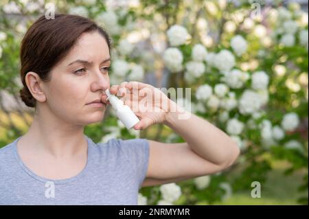 Kaukasische Frau verwendet ein Nasenspray, während sie im Park spazieren geht. Stockfoto