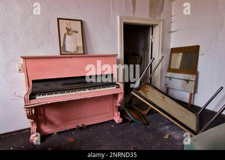 Verlassenes Wohnhaus: Helles Zimmer mit einem alten, blassrosa Klavier, auf dem ein altes Bild eines Zimmermädchens zu sehen ist. Stockfoto