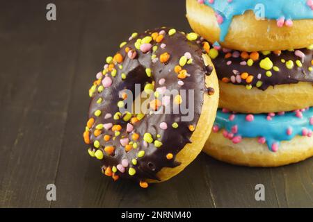 Leckere glasierte bunte Donuts auf einem dunkelbraunen Holztisch. Street Food-Konzept. Nahaufnahme, horizontaler Hintergrund kopieren. Stockfoto