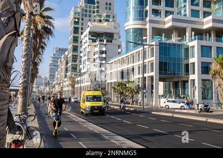 Tel Aviv, Israel - 20.07.2022, Skyline und Sandstrände von Tel Aviv bei Sonnenuntergang. Ein Mann fährt mit einem Motorroller auf einem Radweg am Strand entlang. Stockfoto