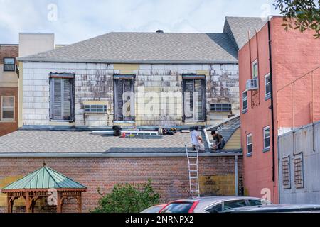 NEW ORLEANS, LA, USA - 22. FEBRUAR 2023: Zwei Arbeiter, die eine Dachrinne auf dem Dach eines alten Gebäudes installieren Stockfoto