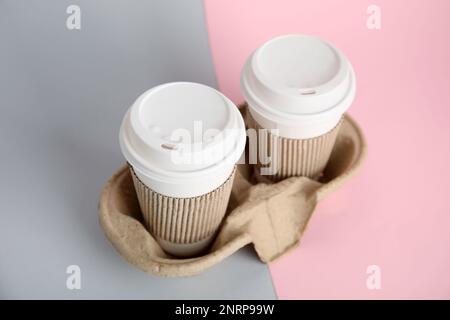 Pappkaffeetassen zum Mitnehmen mit Ärmeln und Kunststoffdeckeln im Papphalter auf farbigem Hintergrund Stockfoto