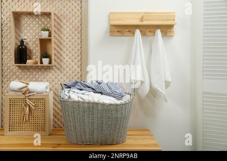 Korb aus Korb mit dreckiger Wäsche auf Holztisch im Badezimmer Stockfoto