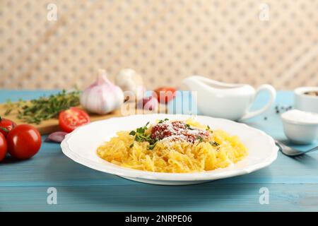 Leckerer Spaghetti-Kürbis mit Tomatensoße, Käse und Thymian auf einem hellblauen Holztisch Stockfoto