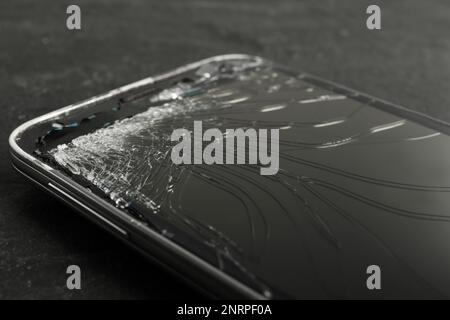 Smartphone mit rissigem Bildschirm auf schwarzem Tisch, Nahaufnahme. Gerätereparatur Stockfoto