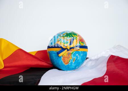 Der mit einem Band verbundene Globus mit der Flagge der Ukraine liegt auf den Flaggen Deutschlands und Polens auf weißem Hintergrund Stockfoto