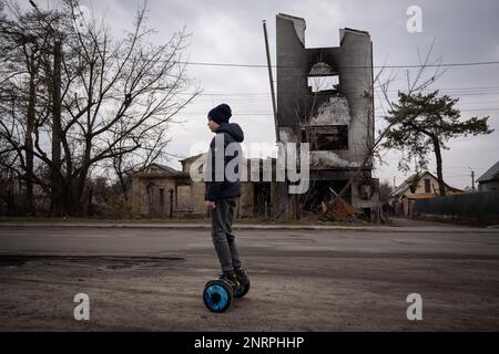 Kiew, Ukraine. 25. Februar 2023. Kiew, Ukraine - 25. Februar 2023: Ein Junge auf Elektrorädern fährt an zerstörten Gebäuden in Irpin, nördlich der Hauptstadt der Ukraine, Kiew vorbei. (Foto: Kish Kim/Sipa USA) *** Korea out *** Kredit: SIPA USA/Alamy Live News Stockfoto