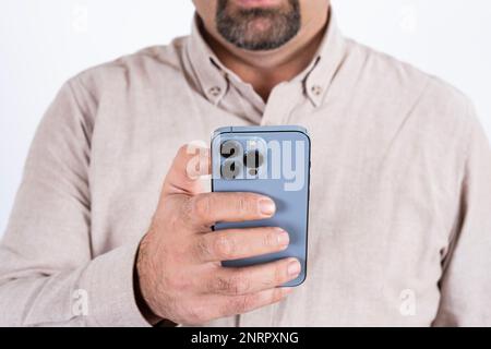 Zugeschnittenes Bild eines Mannes mit einem modernen Smartphone. Blaues Handy mit drei Kameras. Isoliert auf weißem Hintergrund. Das Handy mit einer Hand halten. Stockfoto