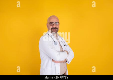 Das Porträt des weissen lächelnden Arztes. Medizinische Karrierekonzeption. In die Kamera schauen. Standstudio mit warmem orangefarbenem Hintergrund. Stockfoto