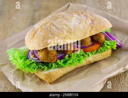 Frisches veganes Sandwich Ciabatta Zwiebeln, Tomaten, Salat, Bohnen Koteletts auf Holzhintergrund. Stockfoto