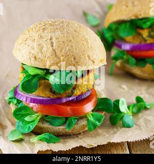 Frisches veganes Sandwich mit Ciabatta-Zwiebeln, Tomaten, Salat, Bohnen-Koteletts auf Holzhintergrund. Stockfoto