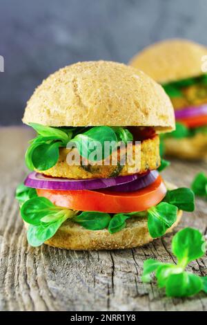 Frisches veganes Sandwich mit Ciabatta-Zwiebeln, Tomaten, Salat, Bohnen-Koteletts auf Holzhintergrund. Stockfoto