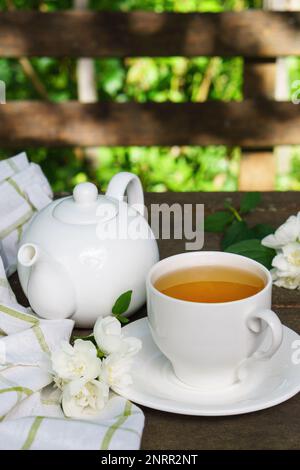 Heißer grüner Tee in einer Teekanne und Tasse mit einem Zweig Jasminblüten und einem weißen Handtuch auf rauem rustikalem braunem Holzhintergrund. Natur gesund s Stockfoto