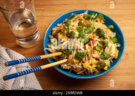 Gebratener Reis mit Gemüse in einer blauen Schüssel mit Essstäbchen, veganisches asiatisches Essen, Draufsicht Stockfoto