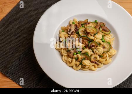 Vegane Pasta mit Zucchini, Pilzen und Erbsen auf einem Teller, Blick von oben Stockfoto