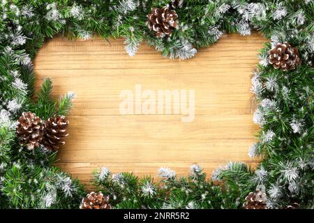 Bogenförmige Weihnachtsgrenze bestehend aus schneebedeckten Tannenzweigen und Zapfen auf weihnachtlichem Holzhintergrund. Hintergrund für Winterferien. Toll für Neuheiten Stockfoto