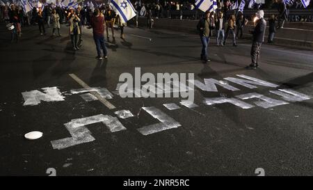 TEL AVIV, ISRAEL - FEBRUAR 25: Regierungsfeindliche Demonstranten mit israelischen Flaggen laufen über ein Graffiti, das "Eine kriminelle Regierung" liest, während sie marschieren und die Autobahn von Ayalon blockieren, Eine der wichtigsten Autobahnen Israels während einer Demonstration gegen die neue rechtsgerichtete Koalition von Premierminister Benjamin Netanjahu und ihre vorgeschlagenen gerichtlichen Änderungen, die darauf abzielen, den Obersten Gerichtshof des Landes am 25. Februar 2023 in Tel Aviv, Israel, zu schwächen. Zehntausende Kundgebungen für die achte Woche in Folge in Israel gegen die weitreichende und umstrittene Reform des israelischen Rechtssystems. Stockfoto