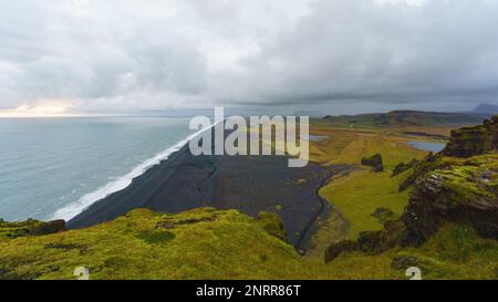 Südinsel, Vik. Blick auf das Meer, das grüne Tal und den schwarzen Sandstrand auf der Halbinsel Dyrholaey. Bereichshintergrund kopieren. Stockfoto