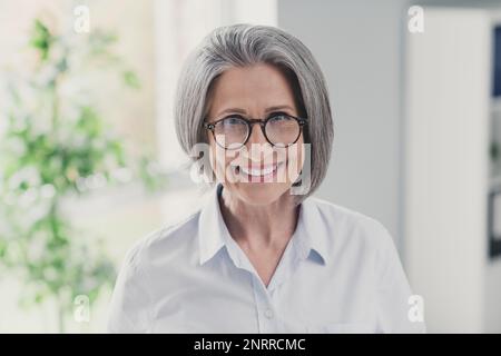 Portrait von intelligenter, fröhlicher, alter Frau, Besitzer einer Firma, Zahnlächeln, Kamera, modernes Bürogebäude im Inneren Stockfoto