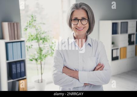 Porträt einer zufriedenen, fröhlichen alten Person, ein Lächeln, die Hände gekreuzt, geräumiges modernes Büro im Inneren Stockfoto